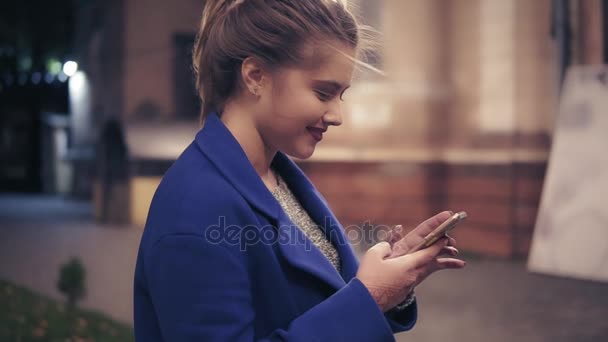 Bella giovane donna che usa il suo smartphone a tarda notte in città. Ragazza attraente sms, navigazione su internet. Luci notturne. Colpo di rallentamento — Video Stock