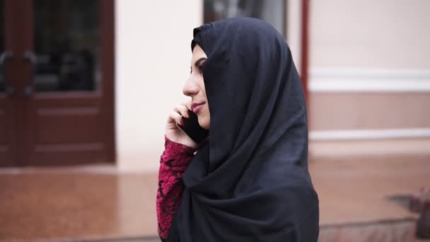 Jonge aantrekkelijke vrouw het dragen van hijab wandelen in de straat in de stad praten op haar mobiele telefoon. Tikje schot — Stockvideo