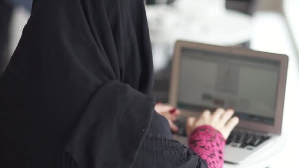 Baksidan på oigenkännlig muslimsk kvinna i svart hijab arbetar på modern laptop på kafé. Studerar eller arbetar. Slowmotion skott — Stockvideo