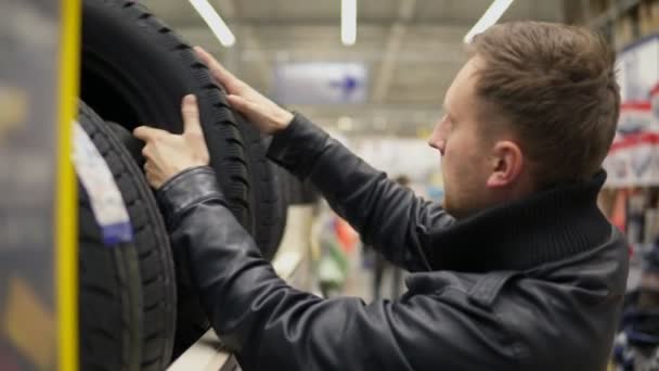 Молодой человек просматривает автомобильные шины в автомобильном отделе гипермаркета и пытается выбрать при нажатии на них — стоковое видео