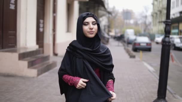 Närbild bild av ung attraktiv kvinna i svart hijab promenader på gatan i staden. Slowmotion skott — Stockvideo