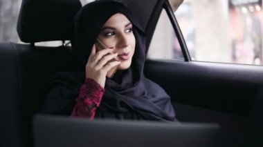 Taksi arka koltukta oturan ve onu laptop tutarken Evet hijab genç çekici Müslüman kadın. Slowmotion atış