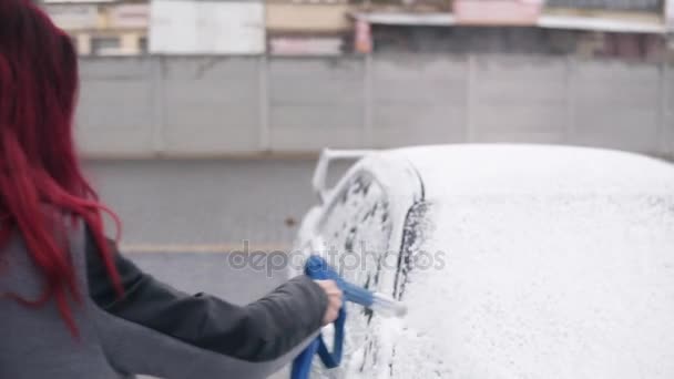 Mujer joven con abrigo aplicando espuma en su deportivo plateado con chorro especial en auto-servicio de lavado de autos — Vídeo de stock