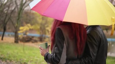 Mutlu çift birlikte renkli bir şemsiye tutan sonbahar Park'ta yürüyordunuz. Deri ceketli çekici adamı sevgilisini benimsemiş. Kızıl saçlı güzel kadın bir kağıt bardak kahve ile tutuyor