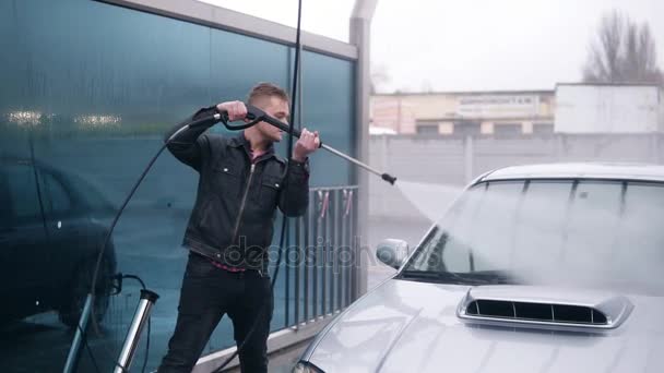 ชายหนุ่มในแจ็คเก็ตหนังล้างรถสปอร์ตสีเงินที่ล้างรถด้วยตนเอง น้ําแรงดันสูงออกมา ภาพเคลื่อนไหวช้า — วีดีโอสต็อก