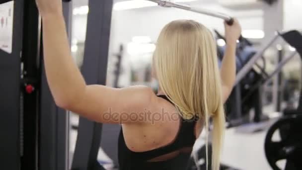 Jolie jeune femme caucasienne blonde avec un entraînement sportif du corps dur sur un lat pull-down mashine à la salle de gym. Concept de mode de vie sain . — Video