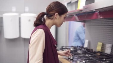 Genç esmer kız mutfak soba cooktop brülörleri düğmeleri presler ve fiyat etiketi ekranından donanım deposunda alır. Ev aleti ekipman seçimi.