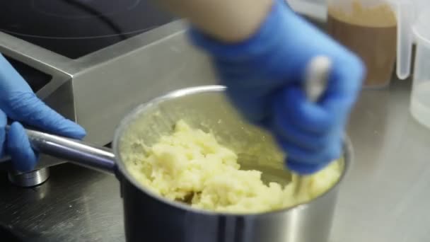 Proces tworzenia parzone ciasto na eclairs lub profiteroles. Ręce cukierników w niebieskie rękawice wymieszać wszystkie składniki razem w garnek stworzyć pyszne ciasto parzone. — Wideo stockowe