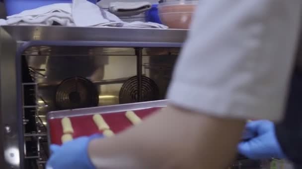 Putting een bakplaat met eclaires of soesjes op het in de oven. Banketbakkers werk. — Stockvideo