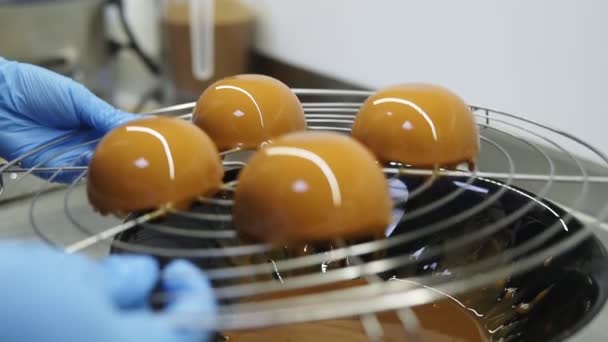 Le mani irriconoscibili del pasticcere in guanti blu portano via un vassoio con torte glassate per finire la preparazione di deliziosi dessert. . — Video Stock