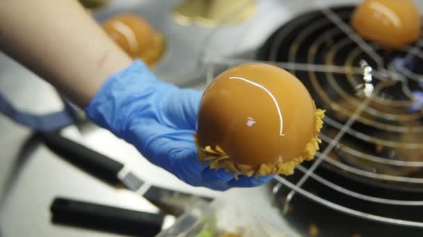 Proceso de creación de deliciosos postres. Las manos irreconocibles de los confiteros en guantes azules decoran pasteles acristalados de caramelo con una capa de patatas fritas en la parte inferior. Imágenes de primer plano — Vídeos de Stock