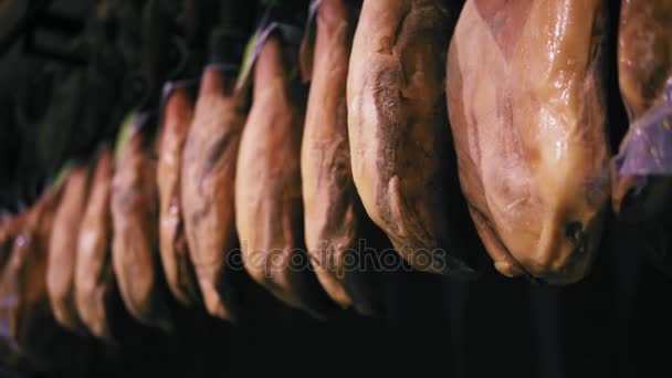 Un metraje slomo de jamón colgado en una fila en el pasillo de carne de la tienda de comestibles. No hay marcas ni lables visibles . — Vídeo de stock