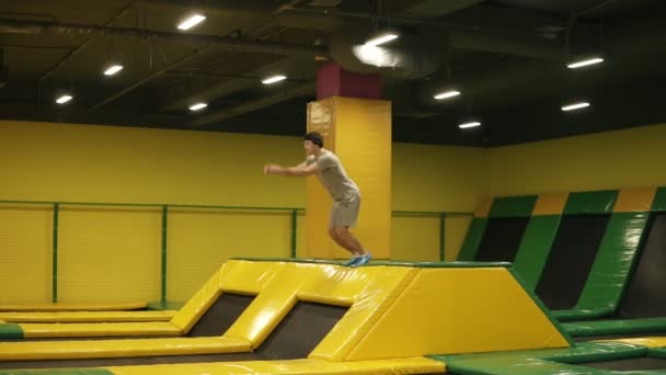 Jovem atleta masculino em camiseta bege e shorts pula no trampolim e gosta de fazer cambalhotas duplos frontais. Juventude, desporto, ginástica . — Vídeo de Stock