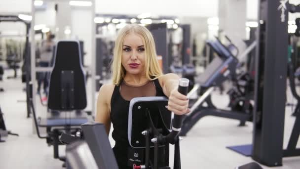 Mujer joven culturista en ropa deportiva negro haciendo exersices en el gimnasio. Construyendo músculos fuertes del núcleo y de los brazos. Imágenes de la parte delantera — Vídeos de Stock