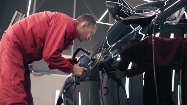 Man in red work suit polishing black car at autocenter. — Stock Video