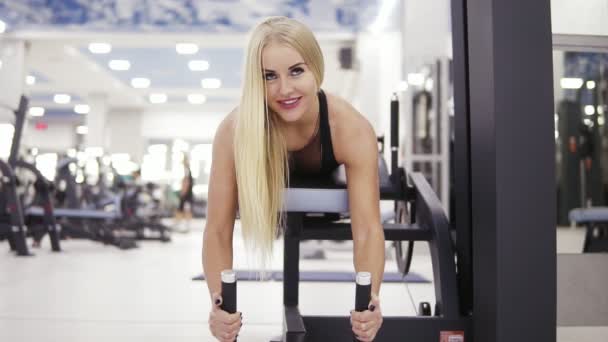 Imágenes frontales de una hermosa chica musculosa sonriendo mientras realiza ejercicios en la mashina de rizos de piernas en el gimnasio. Construyendo un núcleo fuerte. Aptitud y asistencia sanitaria . — Vídeos de Stock