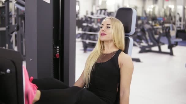 Atrakcyjna młoda blond kaukaski kobieta z sportowy ciała uśmiechający się podczas ćwiczeń na nogi poziome prasy na siłowni. Pojęcie zdrowego stylu życia. — Wideo stockowe