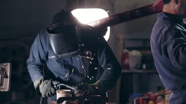 Zaměstnanci v ochranné pracovní oděvy na mechanické hangáru. Dělník v oblasti svařování helmu spojuje dvě kovové kousky. Nebezpečná práce. — Stock video
