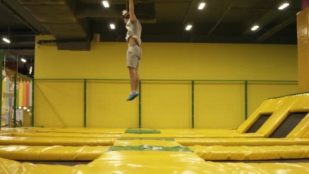 Joven atleta masculino en camiseta beige y pantalones cortos saltando en trampolín con voltereta y escogiendo el cuerpo . — Vídeos de Stock