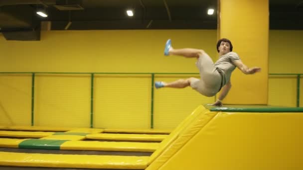 Мужской гимнаст тренируется на профессиональном батуте, прыгает через барьер с поворотом тела и следует за сальто . — стоковое видео