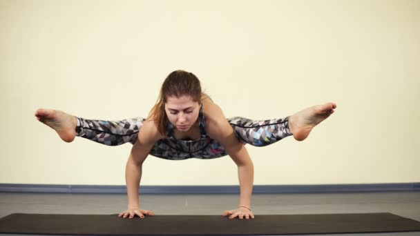 Jonge aantrekkelijke vrouw probeert om evenwicht te bereiken bij het invoeren van een van yoga asanas en het gewicht van het hele lichaam brengen van haar armen. — Stockvideo