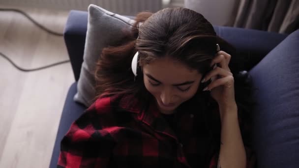 Sexy chica de 20 años está cayendo feliz mientras escucha música en los auriculares con los ojos cerrados . — Vídeo de stock