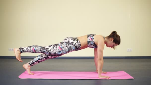 Jeune femme sexy faisant des exercices de jambes en planche horizontale tout en pratiquant le yoga . — Video