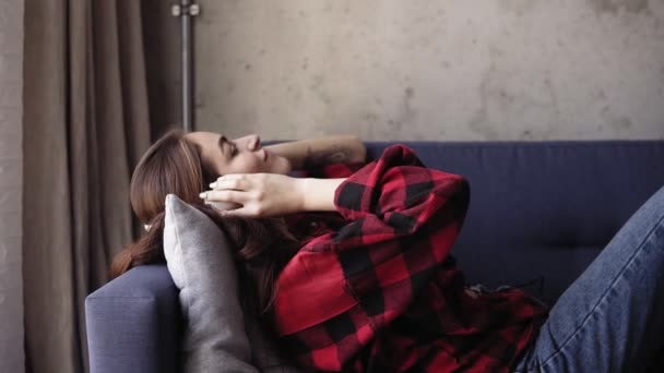 Jovem menina atraente ouvir música enquanto deitado no sofá . — Vídeo de Stock