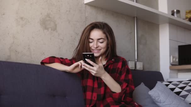 Atractiva chica morena joven sonriendo y desplazándose por el teléfono inteligente . — Vídeos de Stock