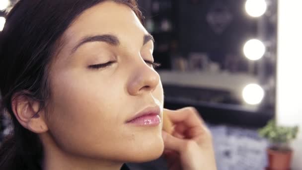 Maquillaje artistas mano aplicando la fundación en la cara previamente preparada de una atractiva chica morena en un salón de belleza o estudio . — Vídeos de Stock