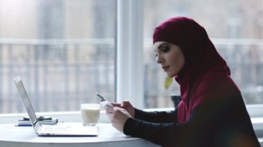 Kapalı çekici bir Müslüman kız smartphone ve dizüstü bilgisayar gibi farklı araçları kullanma görüntüleri