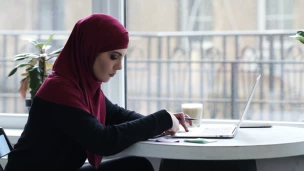Muchacha musulmana joven atractiva con hijab utiliza el ordenador portátil para encontrar información importante — Vídeos de Stock