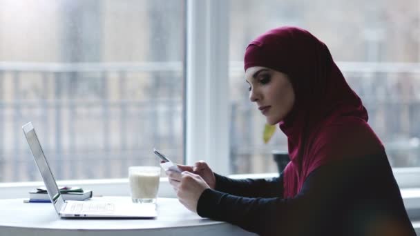 在室内拍摄的一个迷人的穆斯林女孩使用不同的小工具, 如智能手机和笔记本电脑 — 图库视频影像