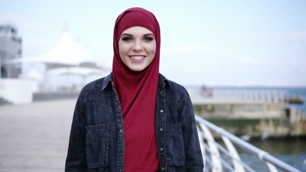 Frontside footage of an attractive young muslim girl with stunning colorful smokey eye make up looking right at the camera while walking near the sea side — Stock Video