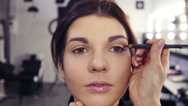 Proceso de llenado de la esquina exterior y pliegue con delineador púrpura. Hermosa chica de aspecto caucásico obtener un maquillaje impecable mirada hecha por un artista de maquillaje en estudio de belleza . — Vídeos de Stock