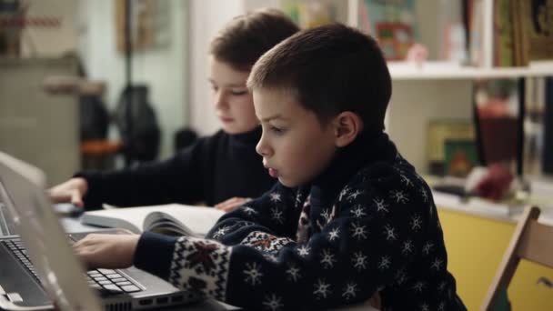 Slow motion bilder av två små pojkar i varma mysiga tröjor sitter i programmering klass framför bärbara datorer, försöker lära sig använda dessa prylar. — Stockvideo