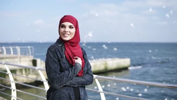 年轻的穆斯林女孩喜欢走近海边与海鸥在背景飞行 — 图库视频影像