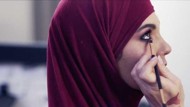 Menambahkan beberapa eyeliner pada garis air mata gadis-gadis cantik. Wanita cantik yang mempesona mengenakan hijab ungu — Stok Video