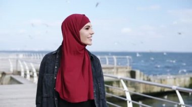 Genç çekici Müslüman kız arka plan üzerinde uçuşan martılar ile bir yürüyüş deniz tarafında yakınındaki sahip sahiptir. Açık havada görüntüleri