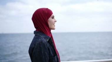 Hijab başında çekici kızı sözde arka plan üzerinde uçan martılar ile deniz tarafında yürüyor