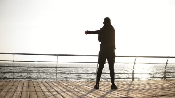 Giovane uomo sportivo che si estende sul molo vicino al mare. Bella mattina di sole sulla costa. Filmati all'aperto. Indietro video . — Video Stock