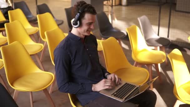 Jovem cara atraente está dançando a música em seus fones de ouvido enquanto trabalhava no laptop . — Vídeo de Stock