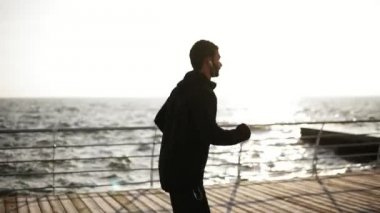 Yan görünümü görüntüleri koşma ya da üstünde belgili tanımlık rıhtım deniz tarafında yakınındaki koşu sportif bir genç erkek. Açık havada görüntüleri.