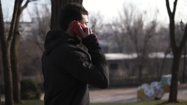 Maschio irriconoscibile che cammina nel parco e parla con qualcuno al telefono . — Video Stock