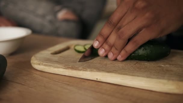 Close-up van slow-motion beelden van een man van de jonge aantrekkelijke vreugdevolle mulat snijden komkommer voor salade dat hes maken voor zijn vriendin nd zelf. Schattig paar doelen. — Stockvideo