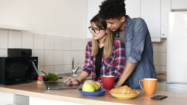 Zeitlupenaufnahmen eines niedlichen Paares, das mit einem Laptop im Internet surft, während es in einer Küche sitzt — Stockvideo