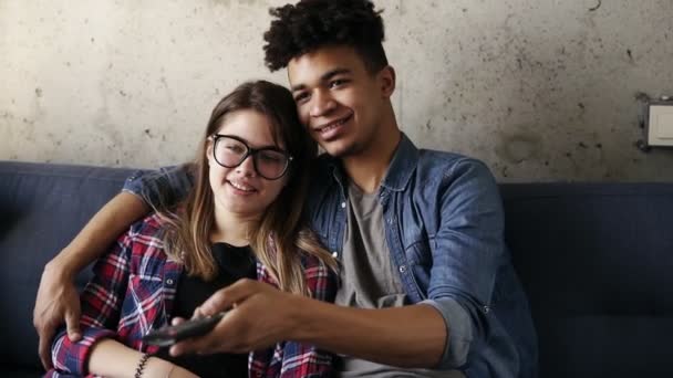 Nettes glückliches Paar junger Hipster, die auf der Couch lächeln und kuscheln, während sie versuchen, einen perfekten Fernsehsender zu finden. Freizeit, Jugend genießen, zusammenleben. Beziehungsziele. — Stockvideo