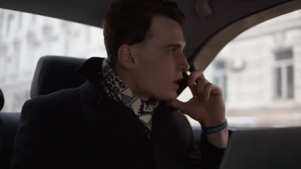 Atractivo chico joven está discutiendo con alguien por teléfono mientras monta en un coche . — Vídeos de Stock