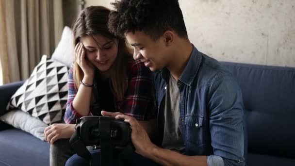 Jovem mulato cara transforma VR-fone de ouvido em e ajuda sua namorada para colocá-lo em . — Vídeo de Stock