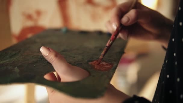 Close up slow motion footage of accurately manicured artist hand spreading oil paint on the palette and adding more color to the painting on easel — Stock Video